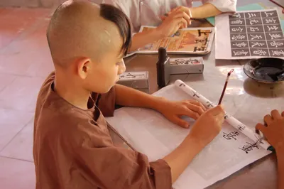 Young boy focused on practicing traditional calligraphy indoors in Hue, Vietnam.