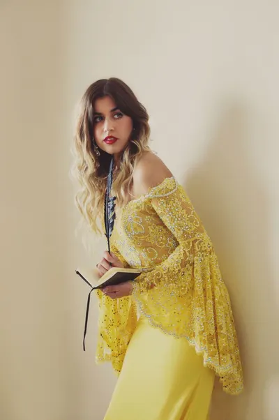 Stylish woman in a yellow lace dress using a feather pen for writing in a notebook indoors.