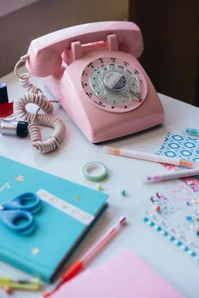 Aesthetic shot of a pink rotary phone and stationery items on a desk.