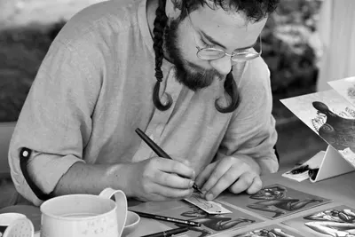 Focused artist creating intricate drawing at an outdoor table in Abano Terme, Italy.