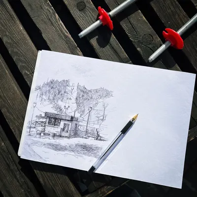 Pencil sketch of a building on a paper sheet placed on a wooden table under sunlight.