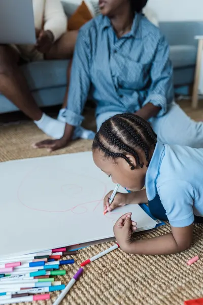 Young child creatively drawing with markers on paper, showcasing artistic expression indoors.
