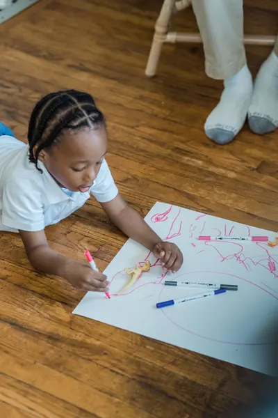 A child lying on the floor drawing with markers, showcasing creative expression and leisure time.