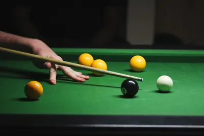 A detailed shot of a player's hand and cue hitting black and yellow billiard balls on a green table.
