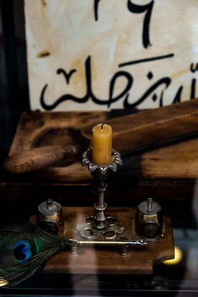 Close-up of a vintage candle holder with Arabic calligraphy, peacock feather, and quill on display.