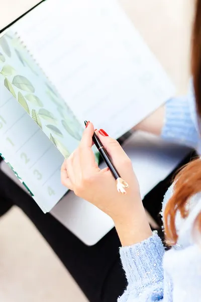 Close-up of a woman writing in a planner with a botanical design, showcasing organization and planning.