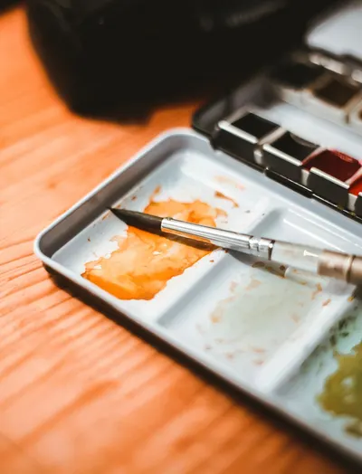 Close-up view of watercolor paints and brush on a wooden table, capturing creativity.