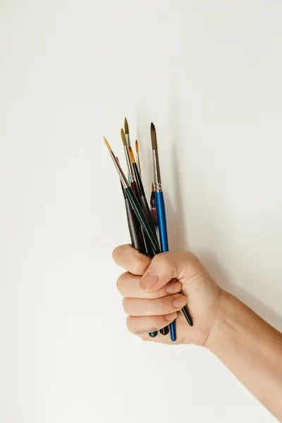 Close-up of a hand gripping assorted paintbrushes, perfect for art-themed concepts.