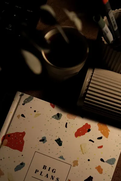 Artistic desk setup with planner, coffee mug, and desk organizers in warm low lighting.