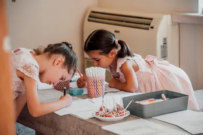 Two young girls focused on drawing with markers at a table, showcasing childhood creativity and concentration.