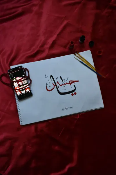 A top view of artistic calligraphy with smartphone on red fabric background.