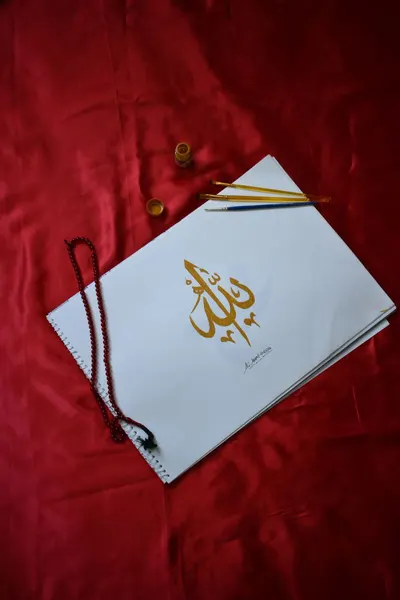 Intricate calligraphy on paper with red beads and brushes, set on a vibrant red fabric background.