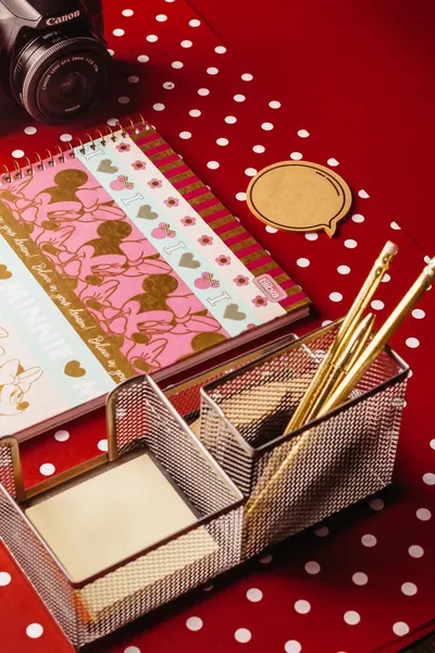 Colorful stationery and camera placed on a red polka dot background, offering a playful workspace look.