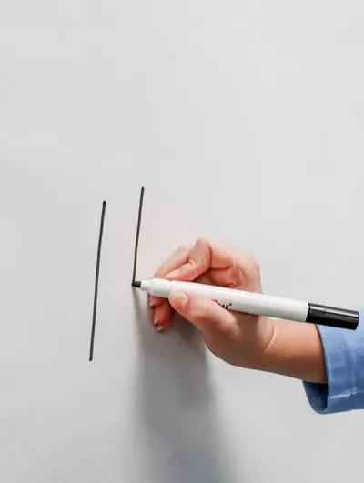 A person's hand drawing lines on a whiteboard with a black marker.