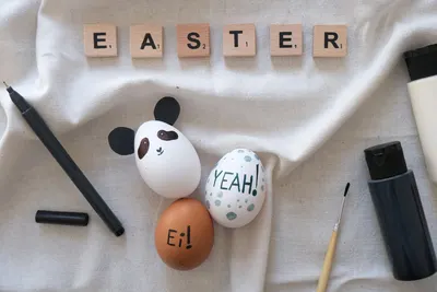Top view of creatively painted Easter eggs with fun messages and designs, surrounded by art supplies.