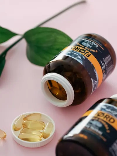 Brown supplement bottles with capsules on a pink background. Includes green leaves for a natural setting.
