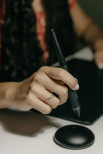 Focused view of a hand holding a stylus while operating a digital drawing tablet, indoors.