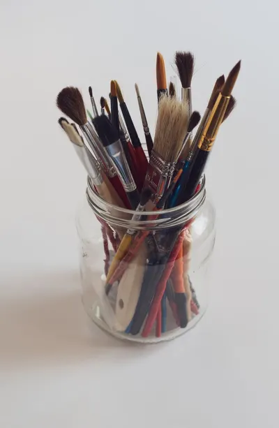 A variety of paintbrushes in a clear glass jar on a white background, representing artistic creativity.