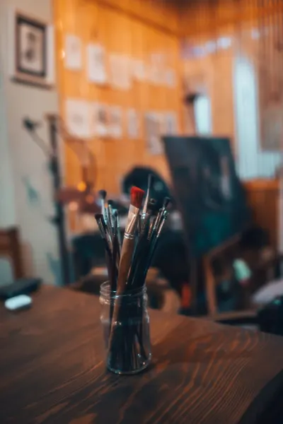 Jar of paint brushes in an artist's studio with blurred background, warm tones.