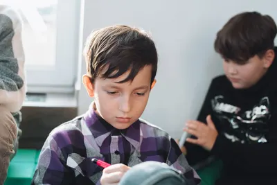 A young schoolboy concentrating while writing with a pen in a classroom setting.