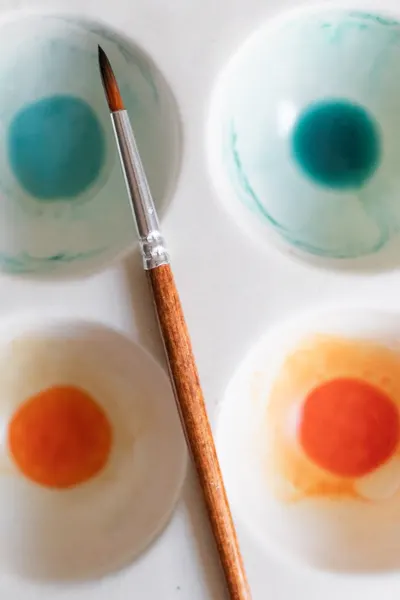 Top view of a watercolor palette with a paintbrush on textured paper.