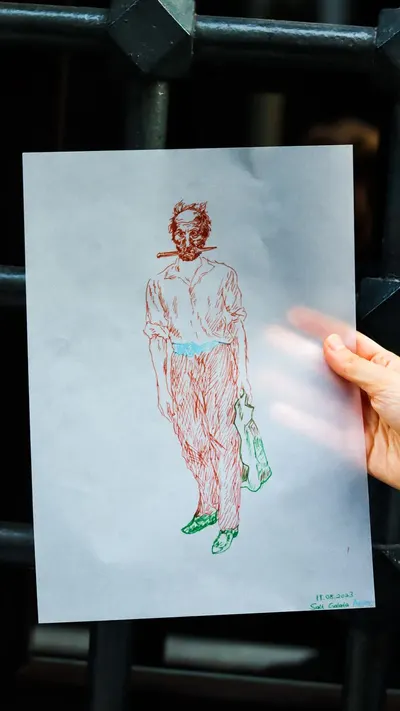 A person holds a hand-drawn sketch of a man near a metal gate in natural light.