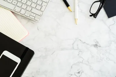 Flat lay of a modern office desk with gadgets and stationery on a marble surface.