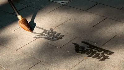 Water calligraphy art on urban pavement with sunlight shadows.
