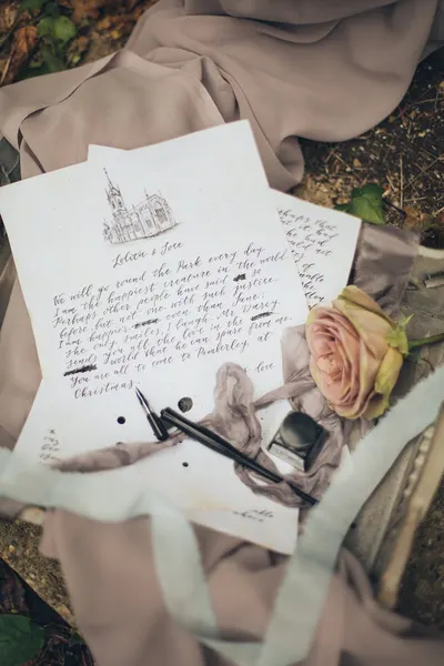 Artistic flat lay featuring handwritten letter, rose, and pen, conveying a vintage aesthetic.