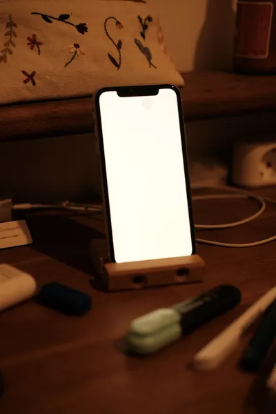 Smartphone on a wooden stand with nearby stationery under warm lighting. Ideal for home office or productivity themes.