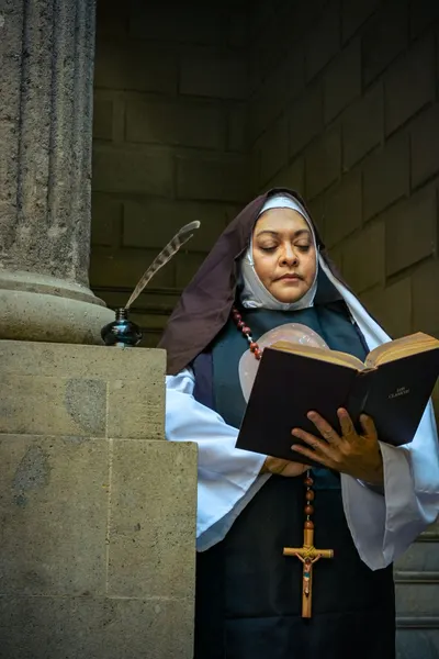 A serious nun reads a religious book dressed in traditional attire with a cross necklace.