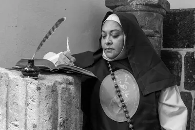 Black and white photo of a nun writing with a quill in Mexico City, depicting religious reflection.