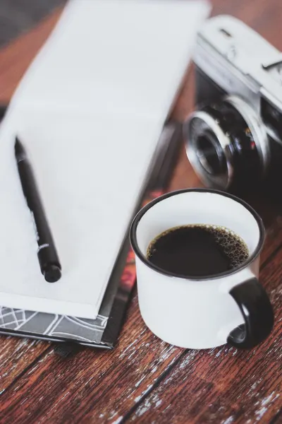 A vintage camera next to a steaming mug of coffee on a wooden surface.