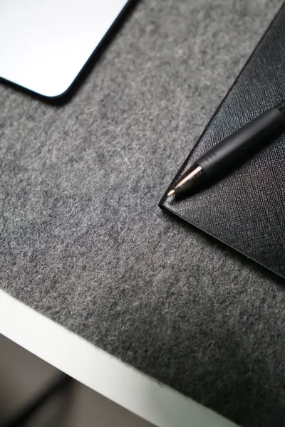 A close-up of a minimalist desk setup featuring a gray pad, notebook, and pen.