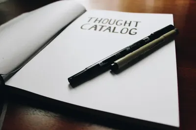 Open thought catalog notebook with pens on a wooden desk, ideal for writing inspiration.