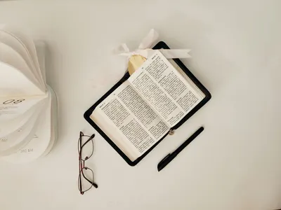 Flat lay of an open book with glasses and pen on a white surface, minimalist style.