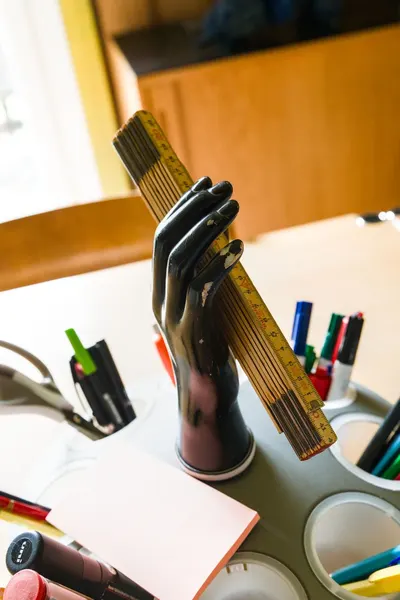 Unique workspace setup featuring a hand-shaped pen holder holding a ruler, surrounded by pens and markers.