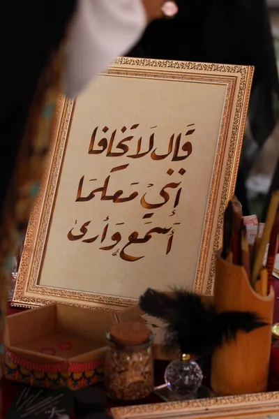 Close-up of Arabic calligraphy in a decorative frame with writing tools.
