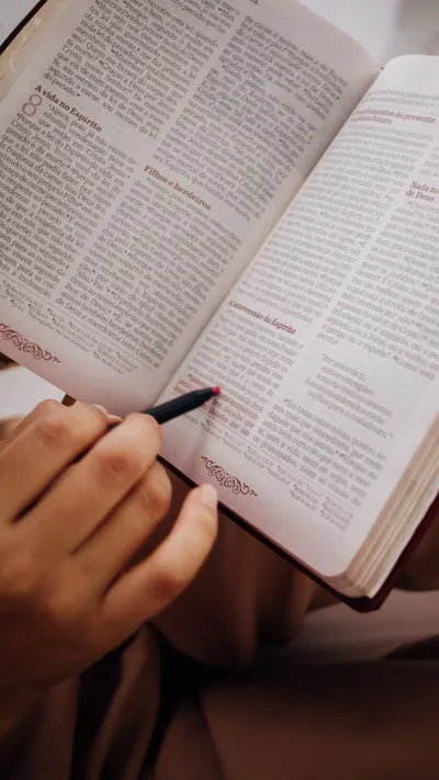 Hand highlights text in an open book with a red marker, focusing on education and learning.