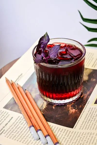 A vibrant iced drink with basil leaves on a magazine page, accompanied by pencils.