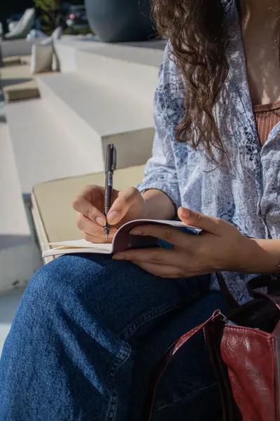 A young woman sitting outdoors in Istanbul, writing in a journal.