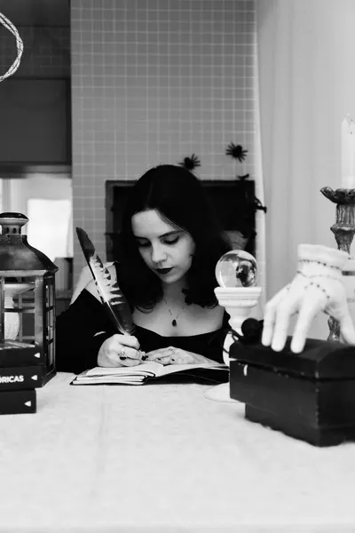 A young woman writes with a quill in a mystical setting with candles and crystals.