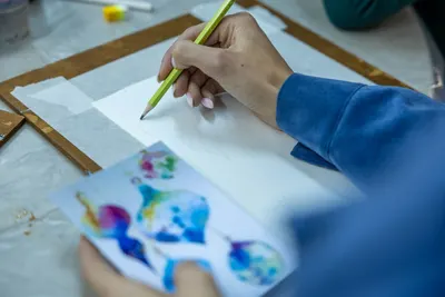 A person sketching a colorful design with a pencil. Creative studio environment.