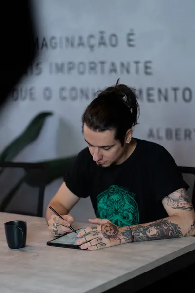 Tattooed artist focuses on digital drawing using a tablet in a modern workspace.
