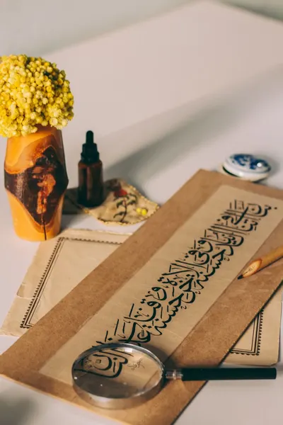 Elegant setup with Arabic calligraphy, magnifying glass, and flowers on a desk.