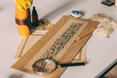 Artistic setup showcasing Arabic calligraphy with magnifying glass and decorative elements on a table.