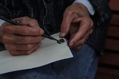 Close-up of elderly hands writing traditional calligraphy, showcasing skill and artistry.