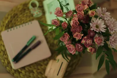 A cozy workspace with elegant pink roses and daisies on a wooden table, creating a warm ambiance.