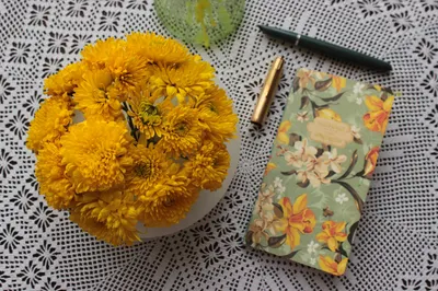 Charming table setting with vibrant yellow flowers, a vintage floral notebook, and a pen on a lace tablecloth.