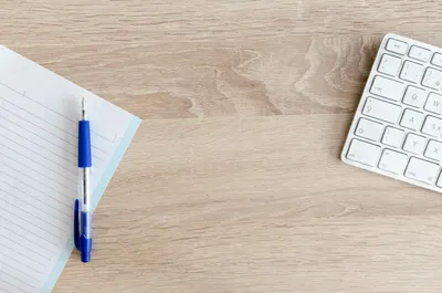 A minimalist workspace with a keyboard, notepad, and pen on a wooden desk.
